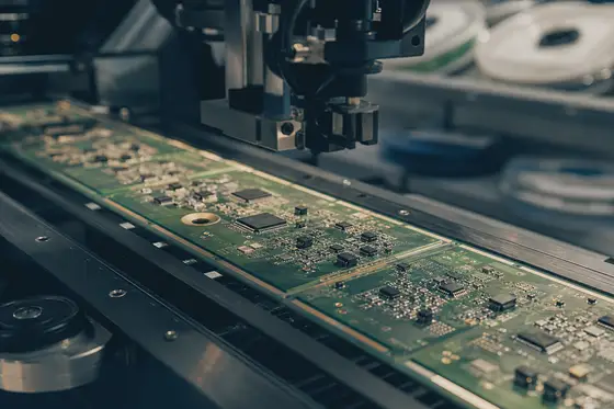 Populated green circuit boards moving through an electronics assembly line beneath a pick-and-place head.